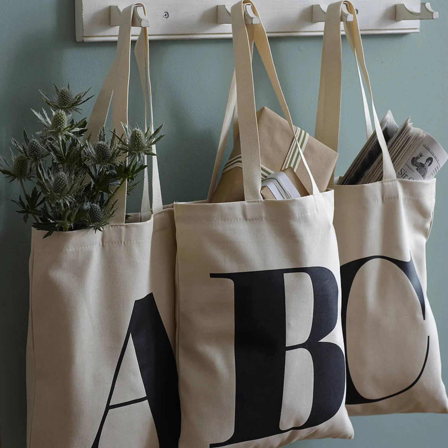 Three canvas tote bags with bold letters A, B, C, hanging on hooks