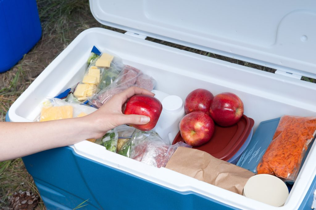 Hand picking an apple from a cooler filled with food items