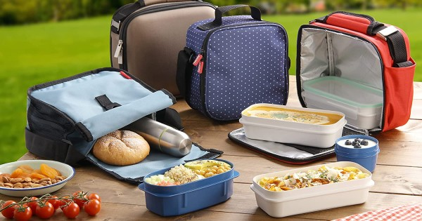 Various insulated lunch bags with meals and snacks on a wooden table outdoors