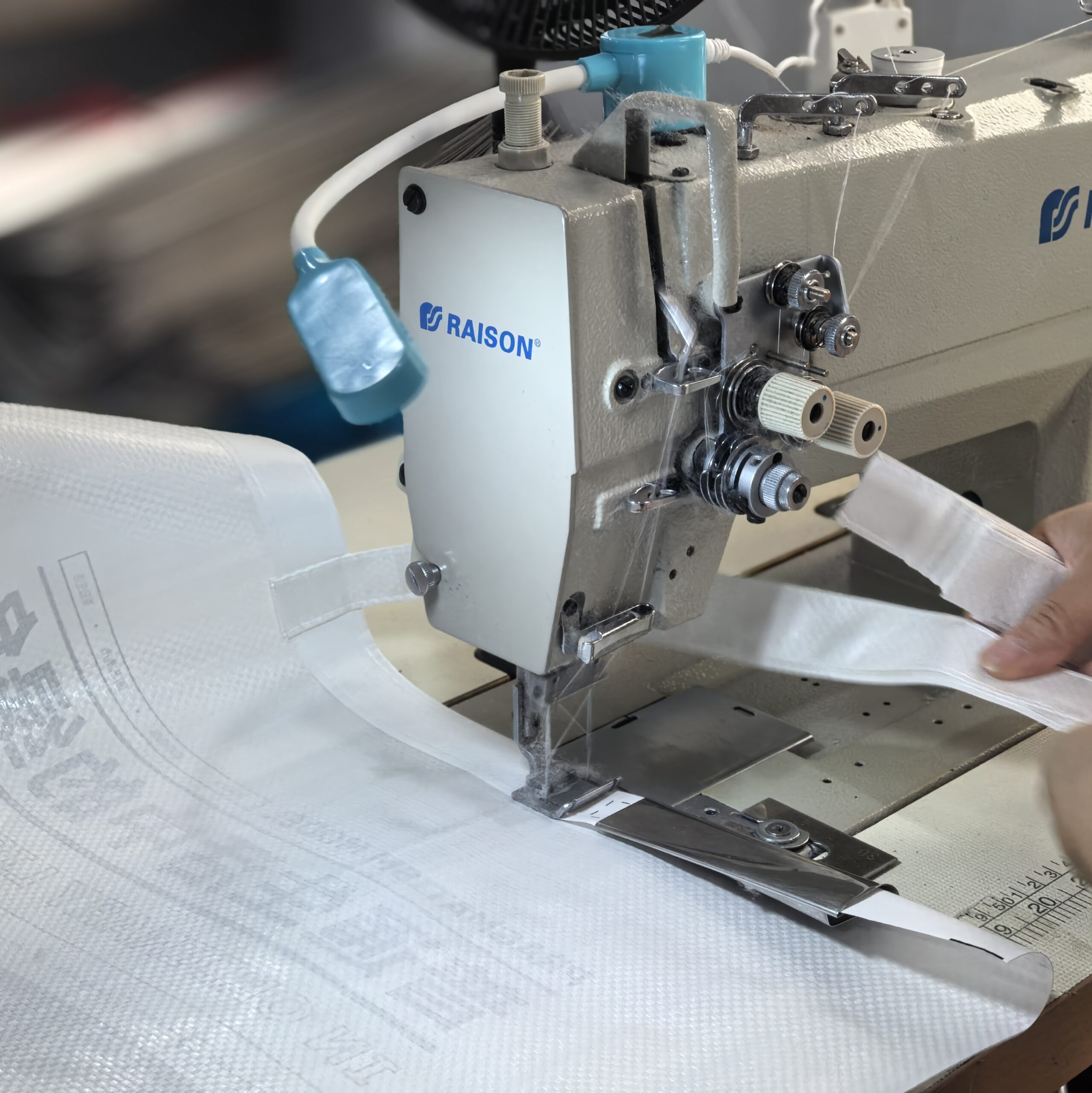 Industrial sewing machine stitching handles onto non-woven shopping bag
