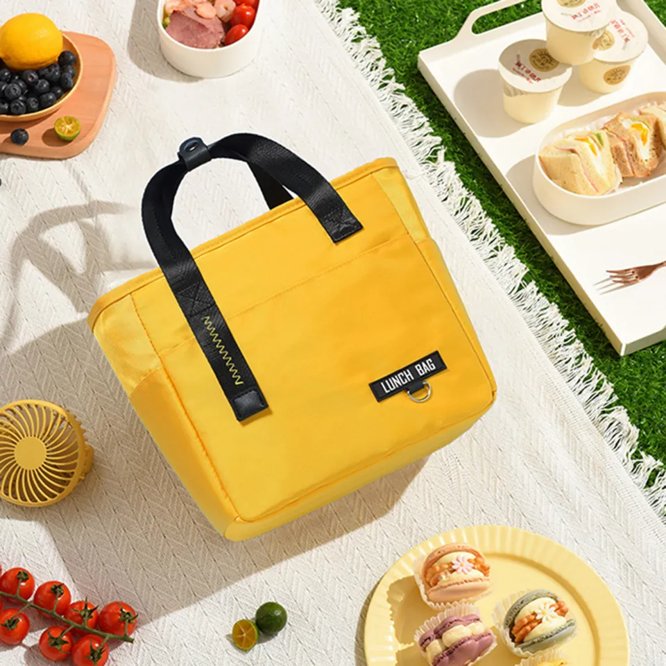 Yellow lunch bag with black handles on a picnic setup, surrounded by food and desserts