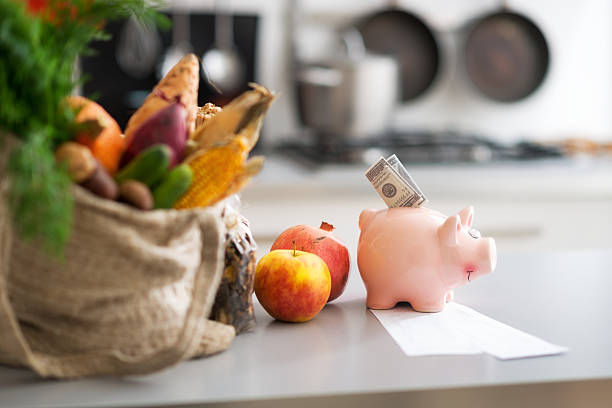 Groceries in a jute bag with a pink piggy bank and apples on a table