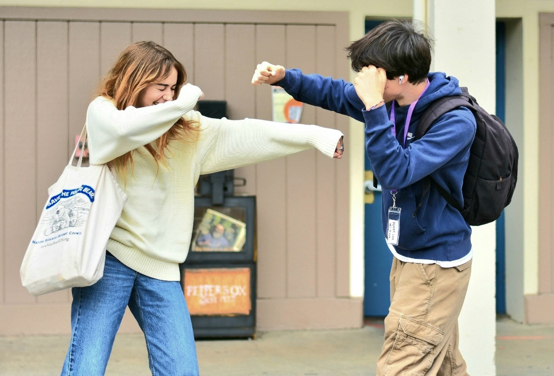 Two students playfully elbow-bumping outside a building