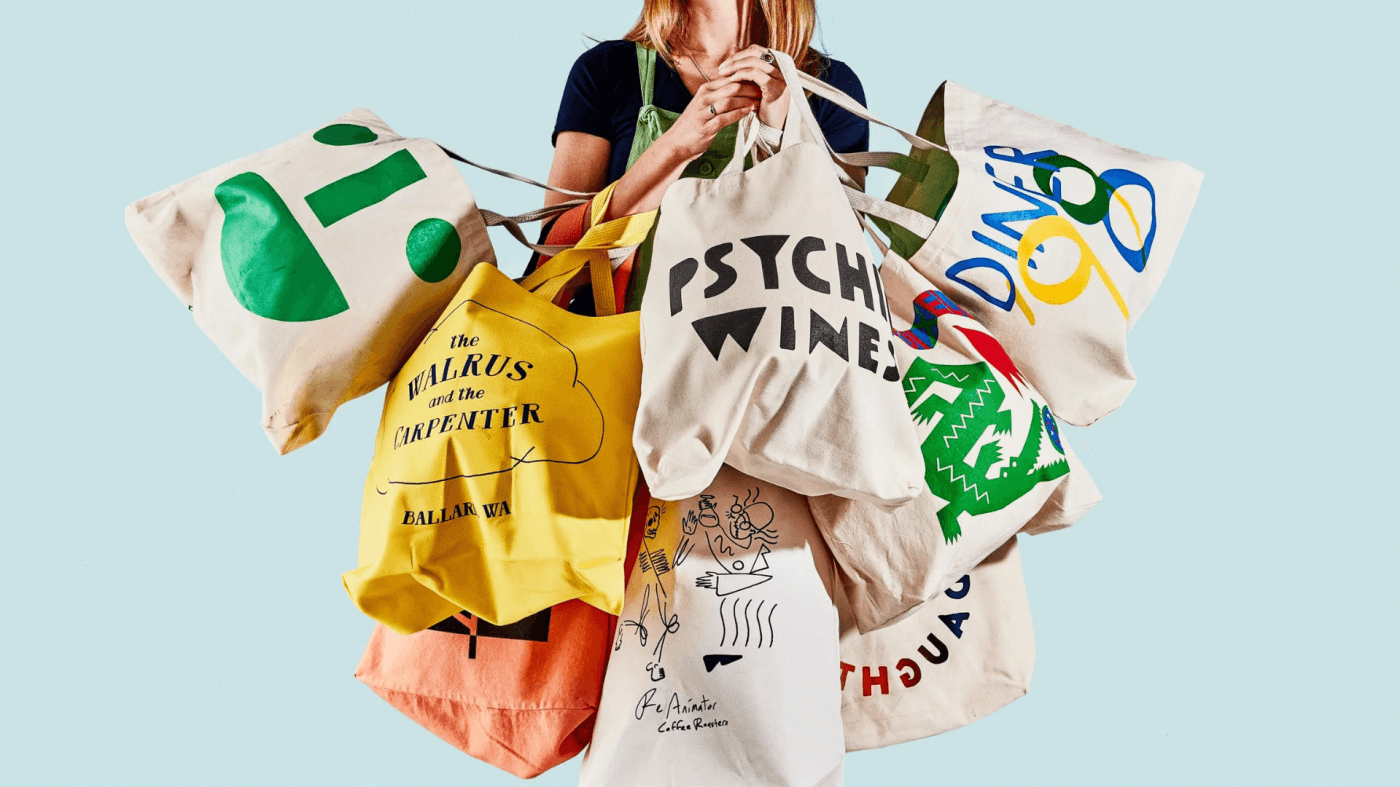 Woman holding multiple colorful reusable tote bags with custom designs