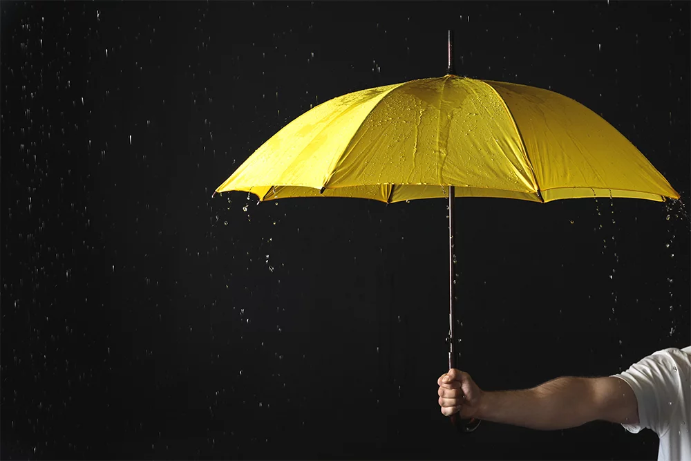 Yellow umbrella held in the rain against a dark background