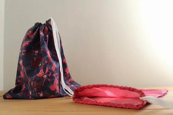 Reusable drawstring bags with floral and pink designs on a wooden surface