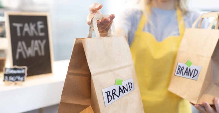 Takeaway paper bags with brand logo, held by a worker in a yellow apron