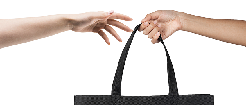 Two hands exchanging a black reusable shopping bag