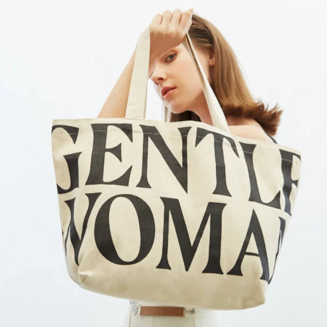 Woman holding a tote bag with "Gentlewoman" printed on it