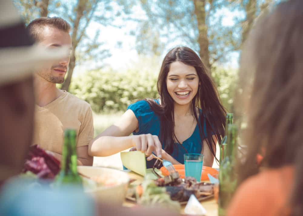 Group enjoying an outdoor picnic, smiling and sharing food under sunlight