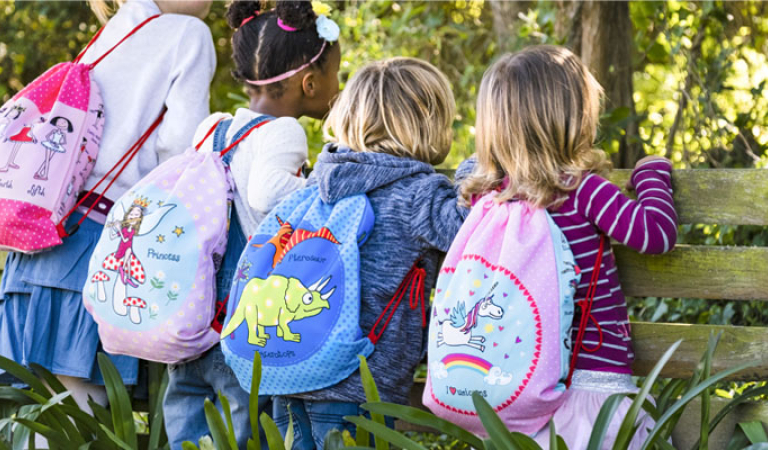 Children wearing colorful drawstring backpacks with fun designs, sitting on a bench