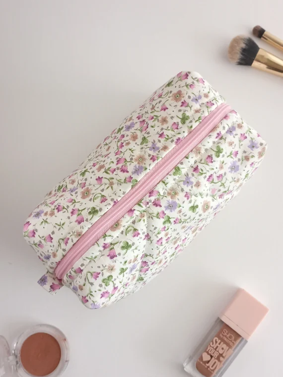 Quilted floral cosmetic bag with pink zipper, surrounded by makeup items