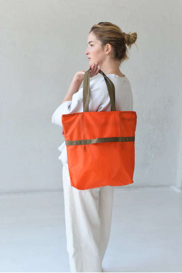 Woman carrying an orange reusable tote bag with green handles