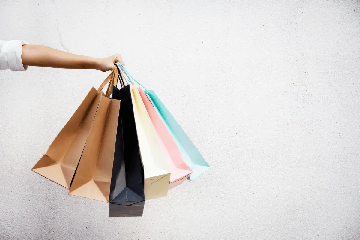 Hand holding multiple colorful shopping bags against a plain background