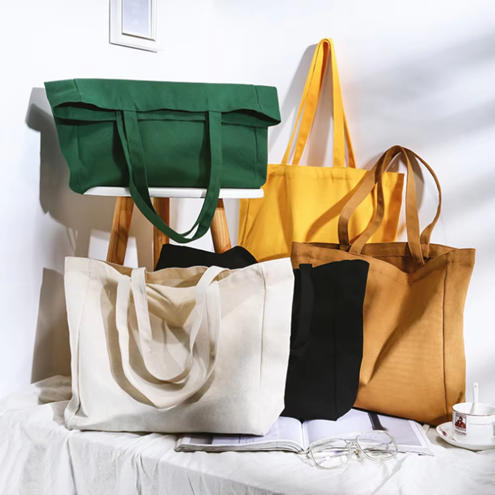 Five tote bags in various colors, displayed on a table with a book and glasses