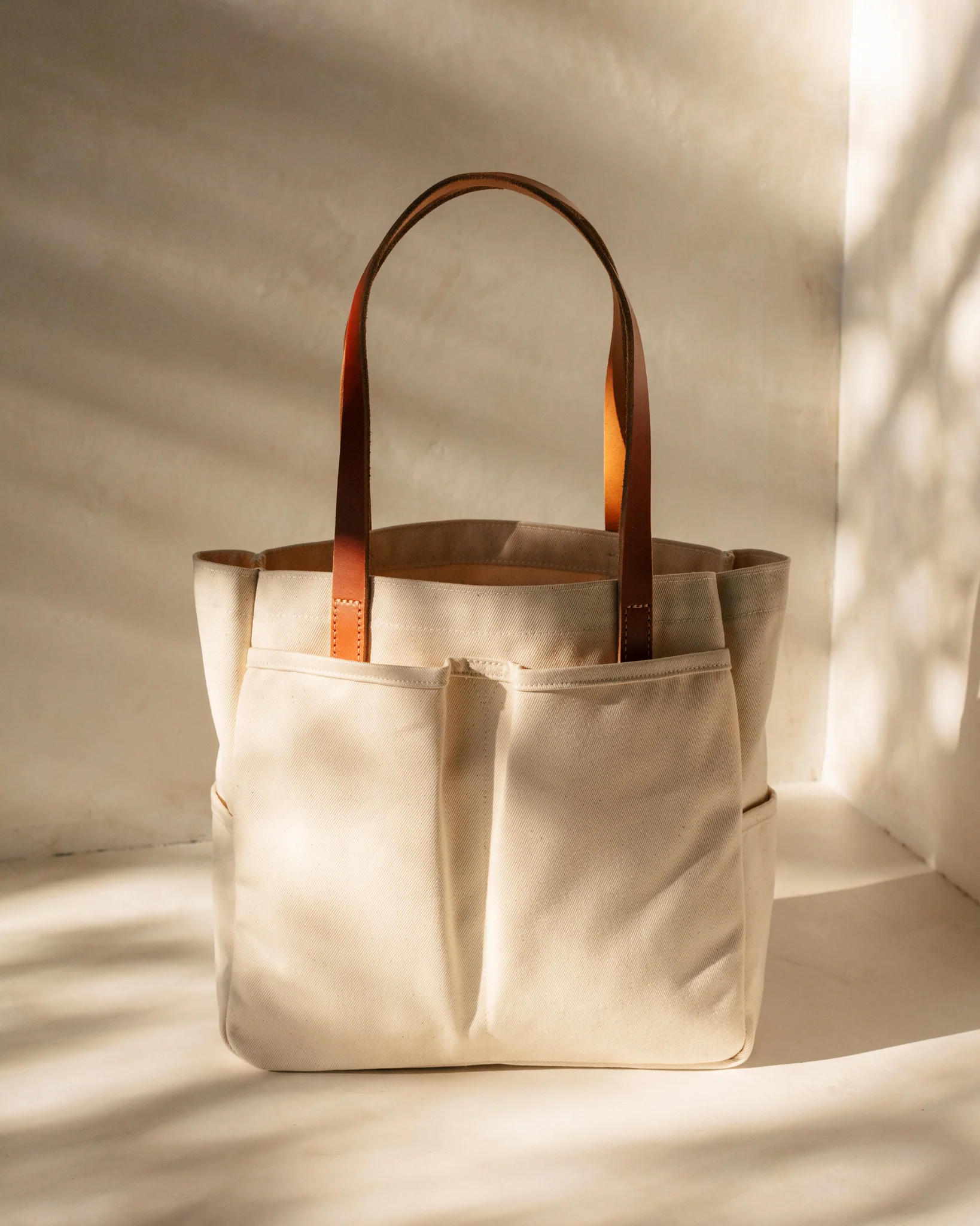 Canvas tote bag with brown leather straps and front pockets, in soft lighting