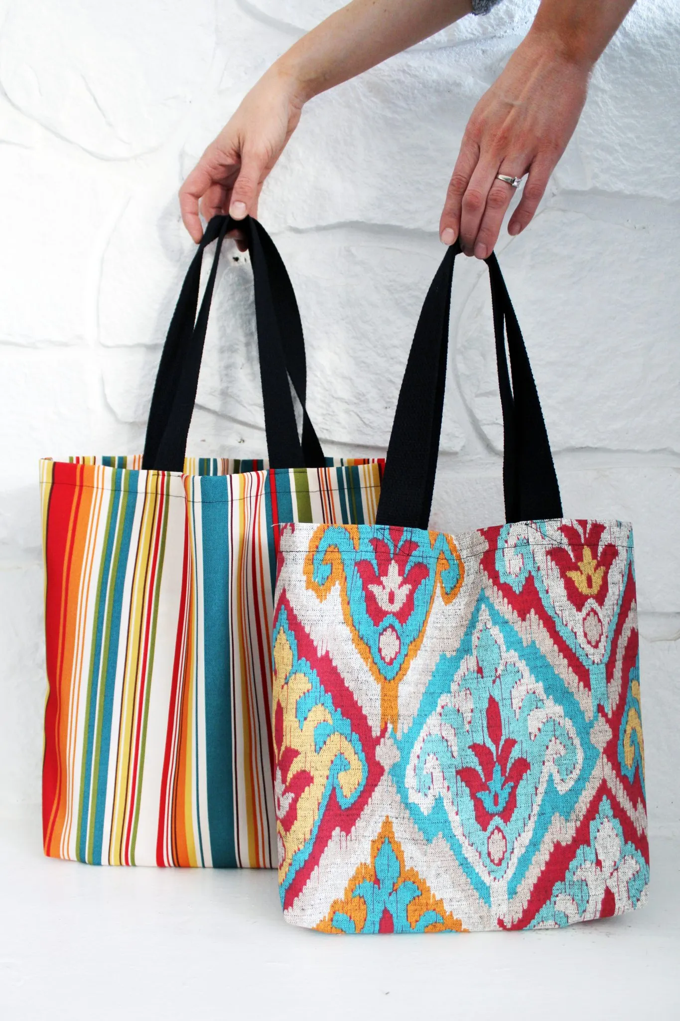 two fabric handbags with colorful patterns and black straps