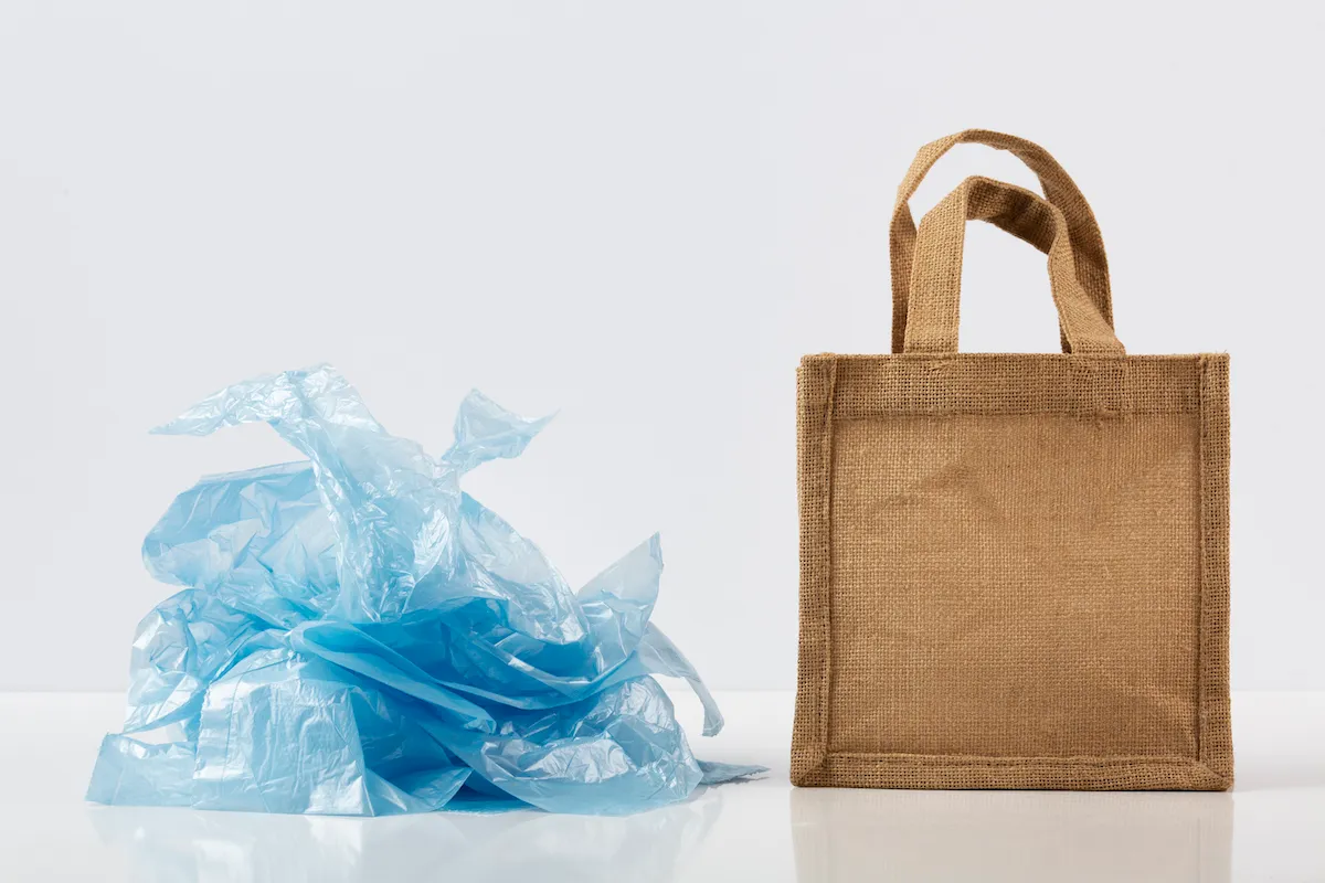 crumpled plastic bag next to a jute reusable tote bag