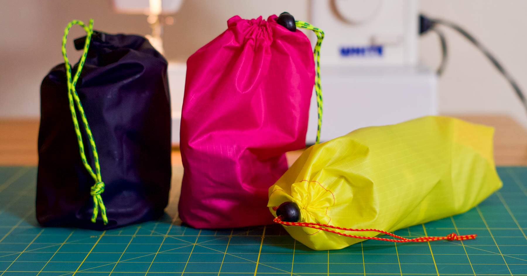 Colorful drawstring bags in purple, pink, and yellow on a green cutting mat