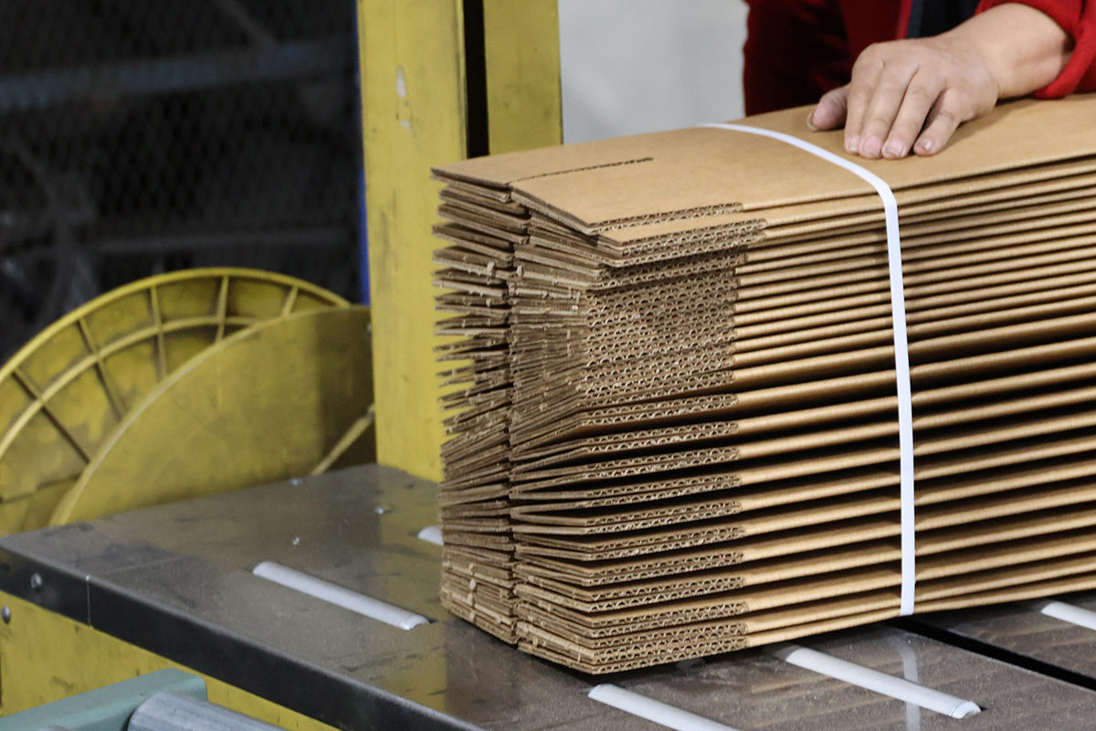 bundle of flat packed corrugated cardboard boxes tied with white strap
