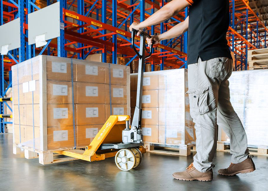 worker moving shrink wrapped cardboard boxes with pallet jack in warehouse
