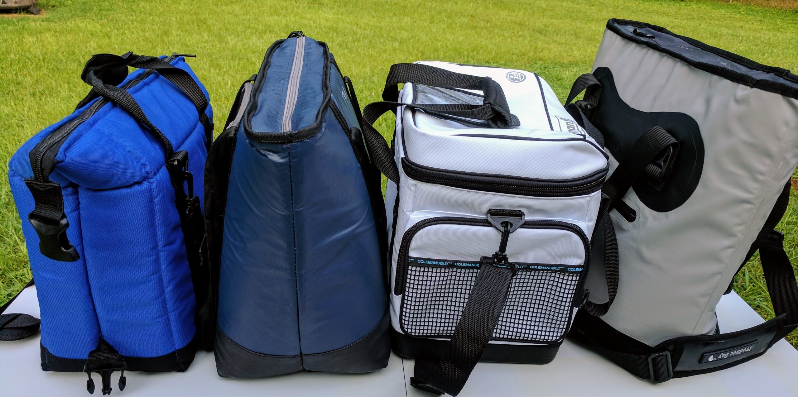Four different insulated cooler bags standing upright on a table outdoors
