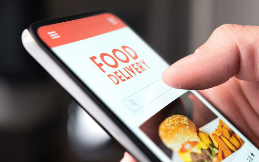 Hand using food delivery app with burger and fries image