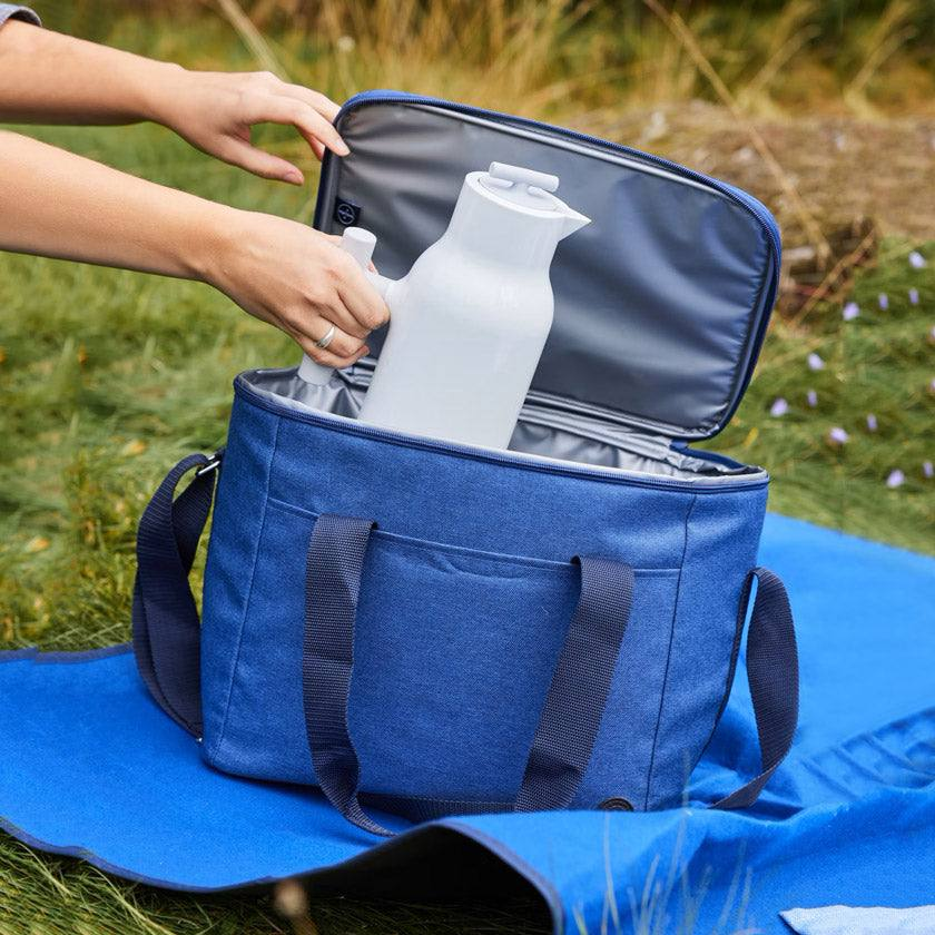 Person placing thermos into blue insulated cooler bag outdoors