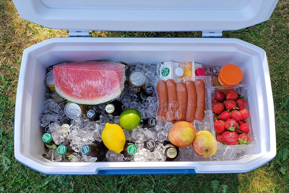 Open ice cooler filled with fruits, drinks, sausages and ice for outdoor picnic