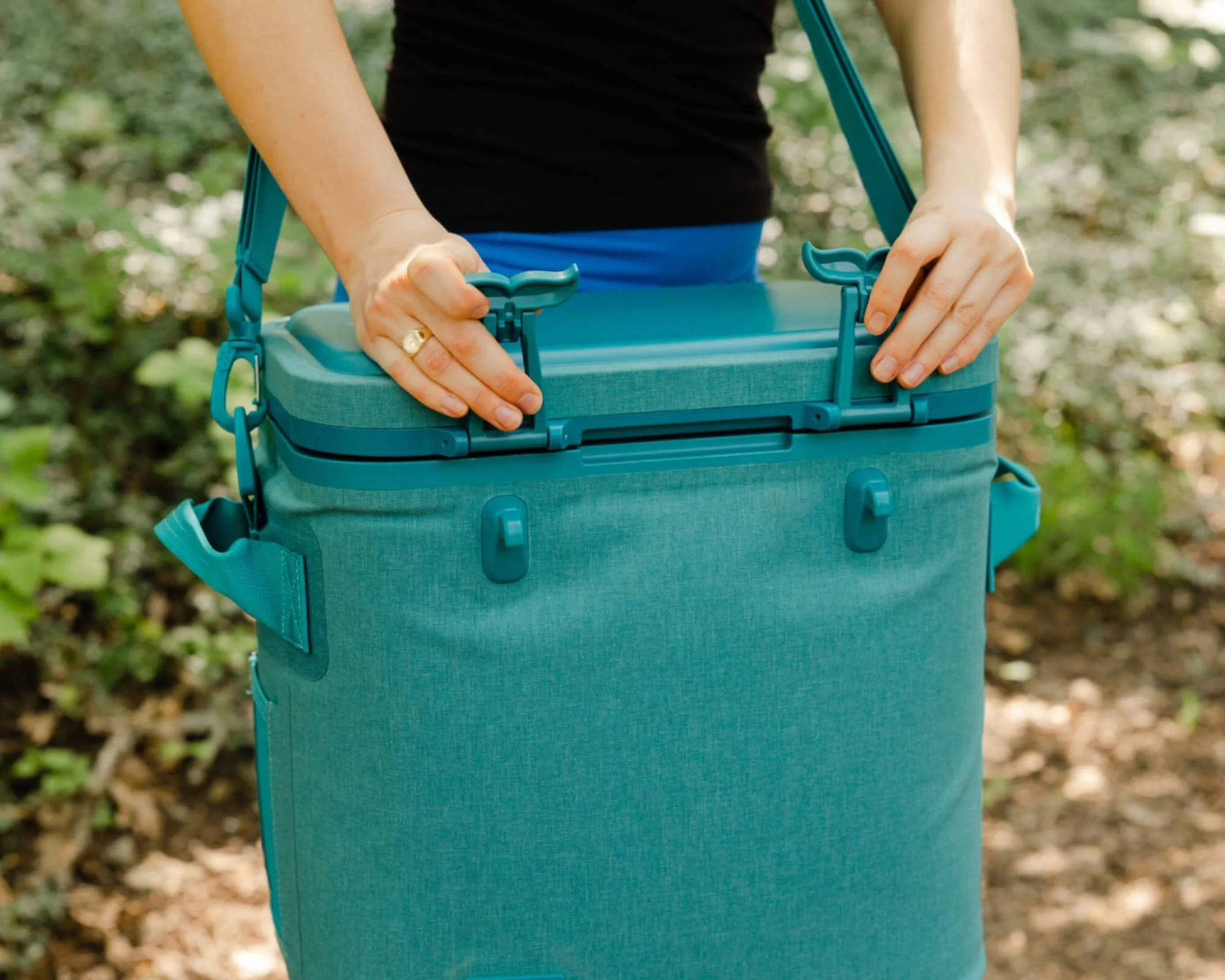 Person securing a teal insulated cooler outdoors