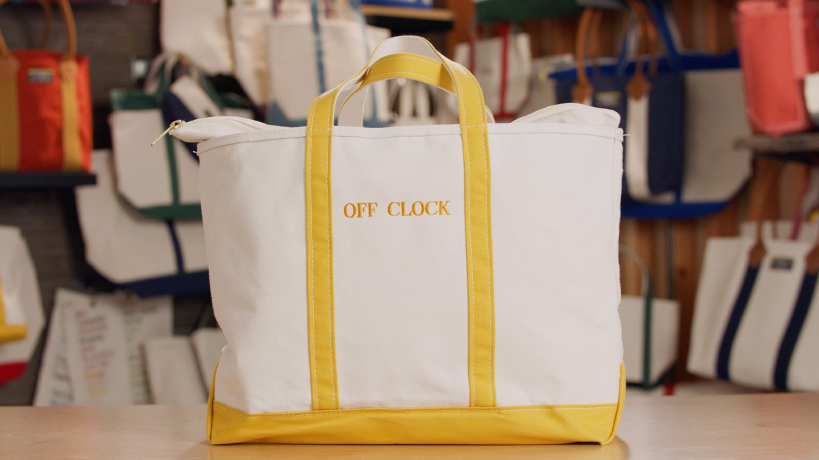 White canvas tote bag with yellow handles and "OFF CLOCK" text