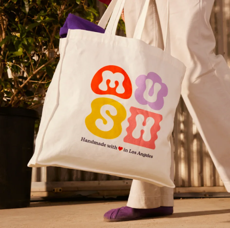 Colorful MUSH print tote bag carried by person in white pants