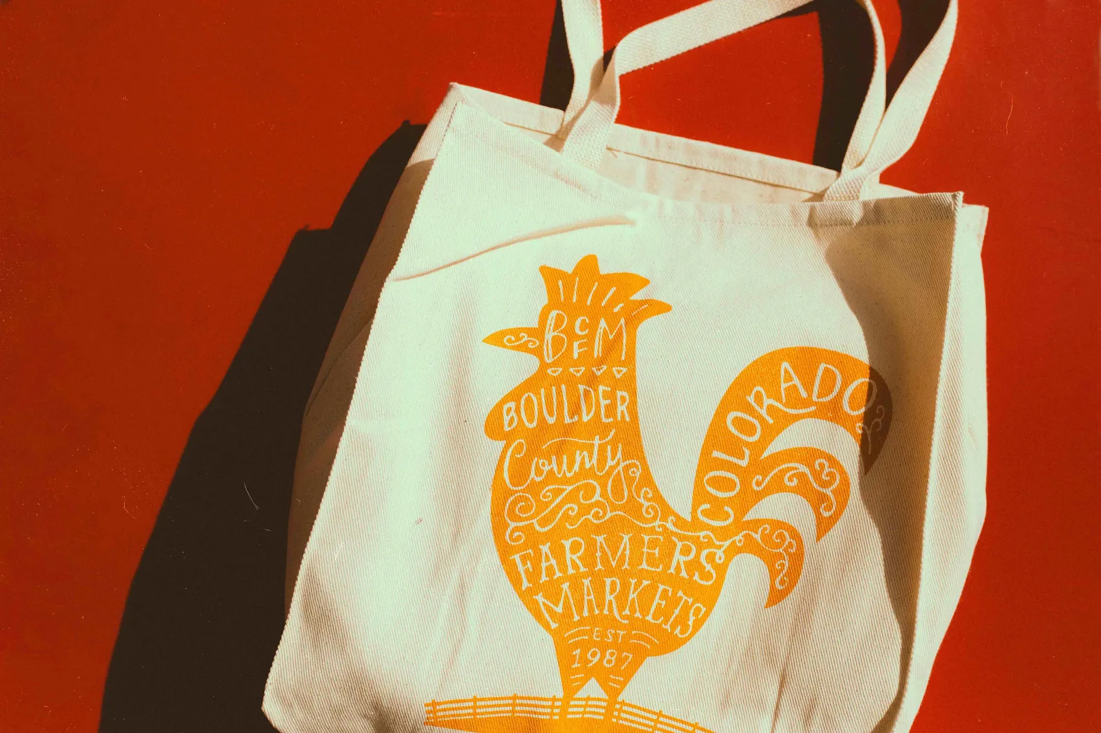 Tote bag with orange rooster graphic and farmers market text