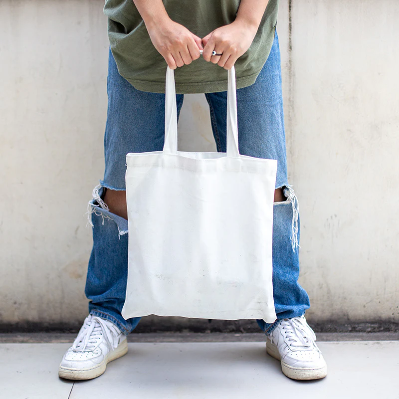 Plain white cotton tote bag held by person in jeans