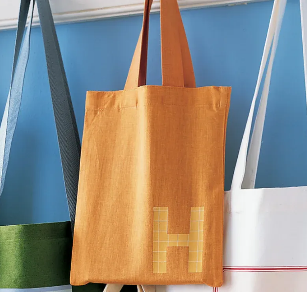 Colorful tote bags hanging, with orange bag featuring a grid-style letter H