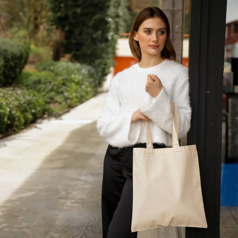 Woman holding blank beige non-woven tote bag outdoors