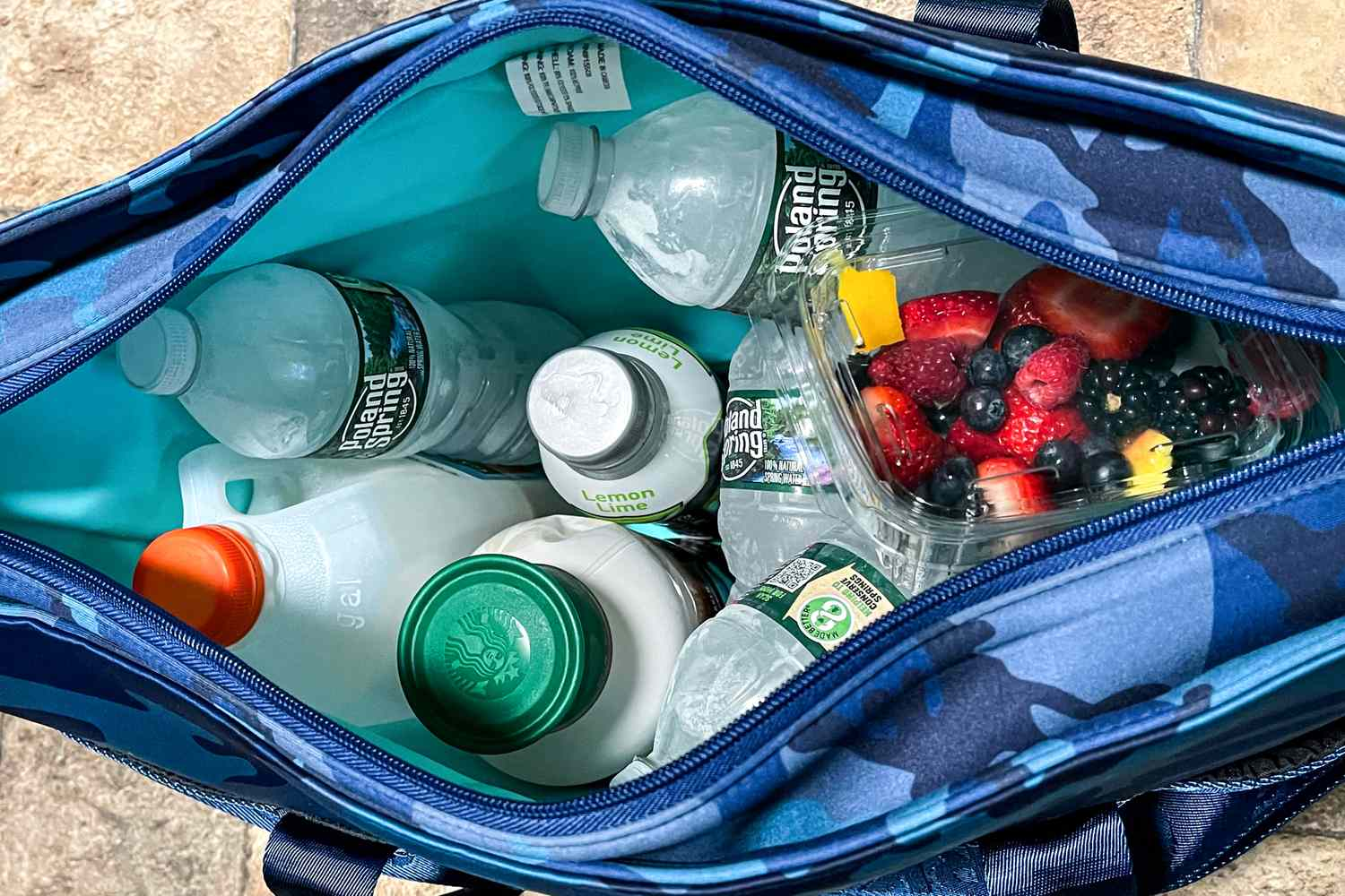 Top view of a blue insulated bag filled with drinks and fresh fruit