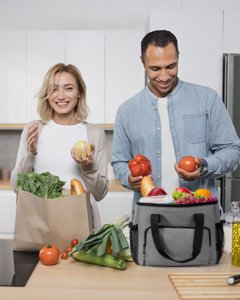 Smiling couple holding fresh produce with reusable grocery bags in kitchen