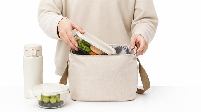 Packing a Personal Lunch Bag A person packing a lunch bag with food containers and a drink