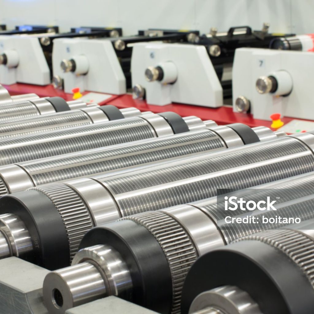 Lined up magnetic cylinders for die cut on rotary printing press. Magnetic cylinder for flexo rotary die cutting. Magnetic roll and in-line press machine in background. Cylinder for cutting dies.