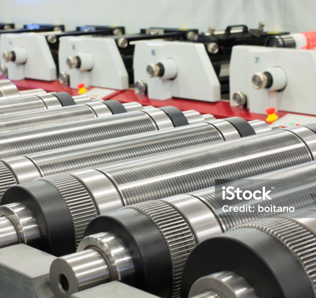 Lined up magnetic cylinders for die cut on rotary printing press. Magnetic cylinder for flexo rotary die cutting. Magnetic roll and in-line press machine in background. Cylinder for cutting dies.